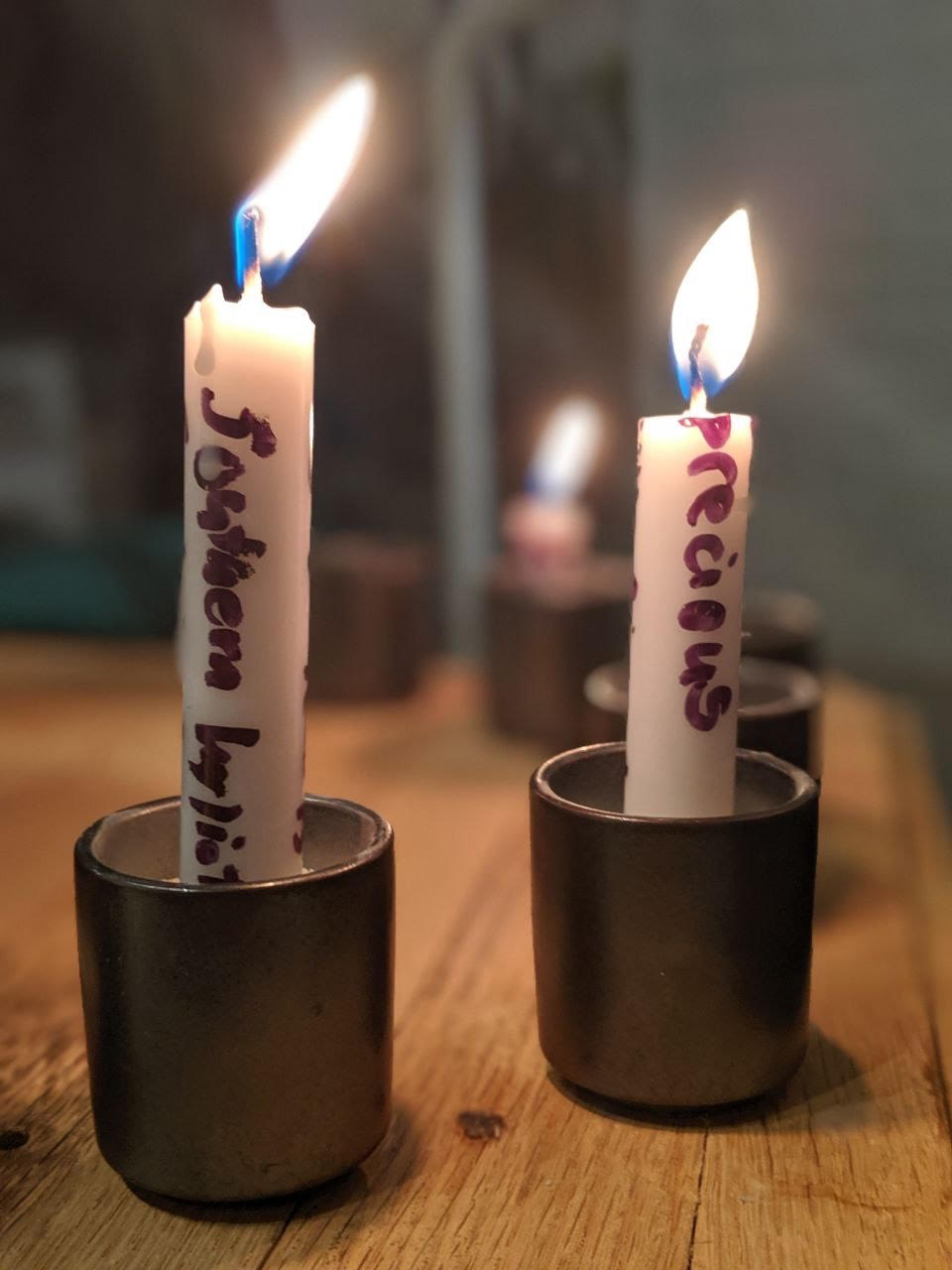 Lit white candles from the Remembering Network shrine with messages written on them in black marker