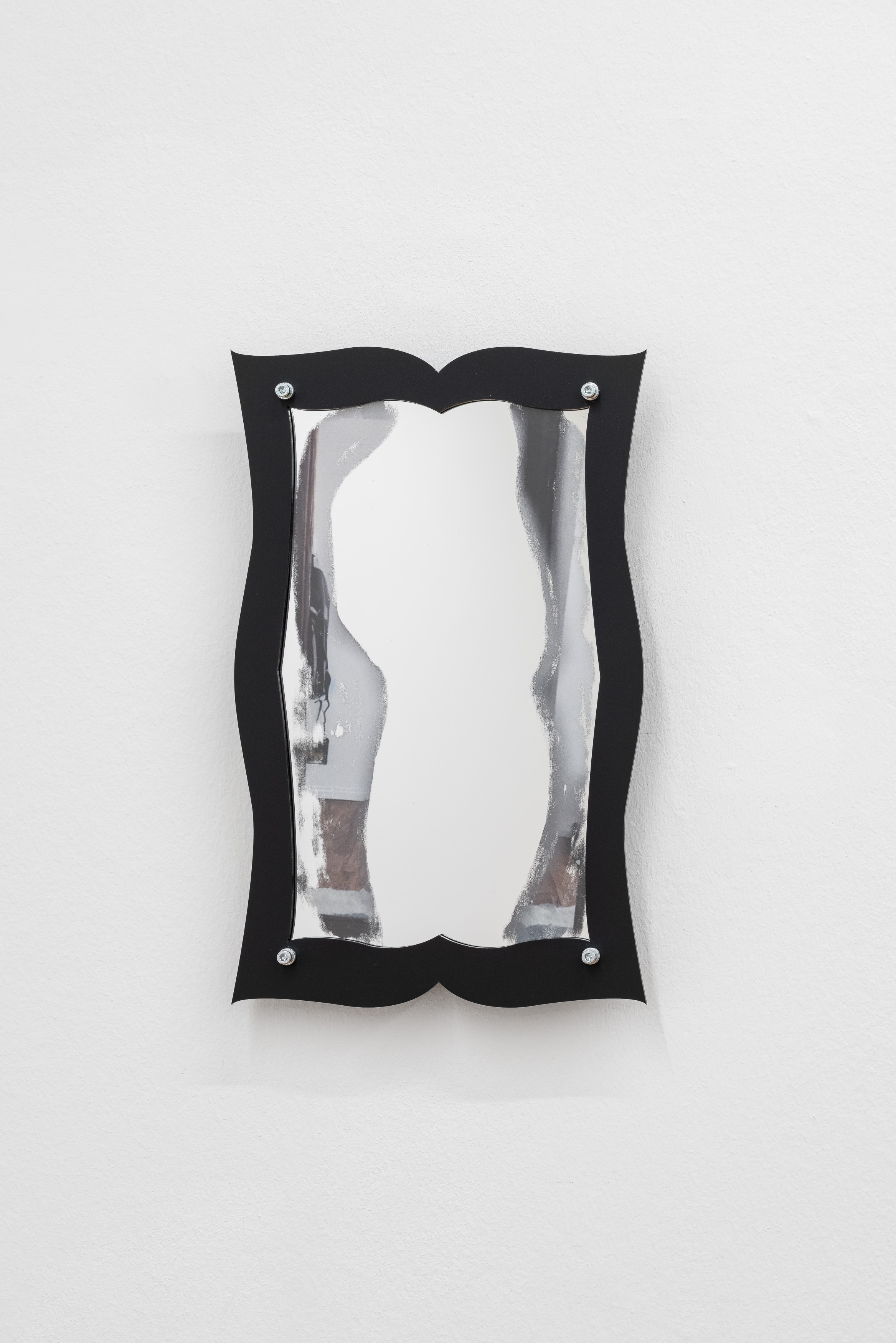 A wall-mounted mirror with a wavy black frame and silver bolt fixings at each corner, its reflective surface showing a smeared, distorted reflection of a body